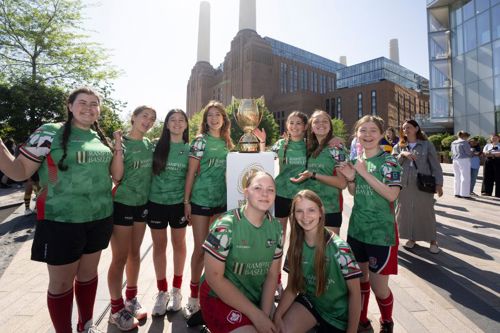 A group of young women rugby players standing around a trophy with Battersea Power Station in the background