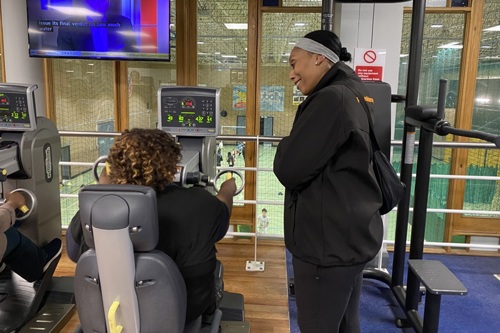 A Places Leisure gym trainer supports Joan as she uses a seated gym machine